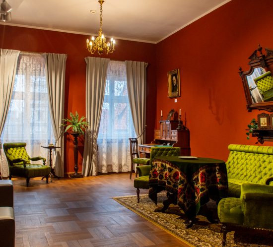 pomieszcznie w Muzeum Literackim Henryka Sienkiewicza: zabytkowy stół, fotele, w tle duże, przysłonięte długimi zasłonami, okna